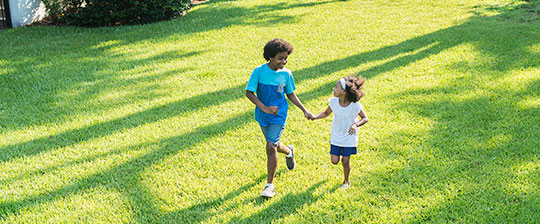 Two kids running through yard holding hands on spring day