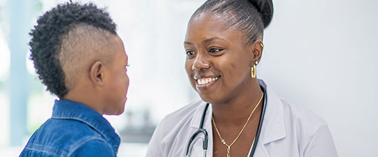 Female doctor smiles as she talks with young boy.