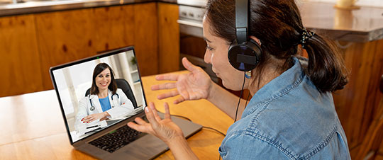 Woman in kitchen on laptop talking with doctor via virtual care