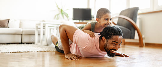 Dad and young son laughing as dad does pushups with son on his back.