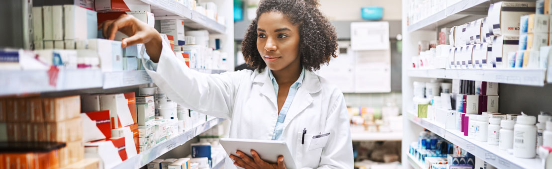 young woman in a lab coat grabbing medicine off of a shelf