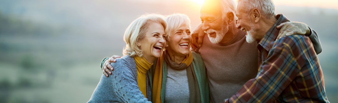 group of mature people smiling and hugging outside during sunset